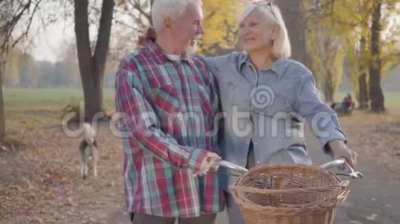 快乐的高白种人家庭站在秋天的公园里骑着自行车和交谈微笑着退休的成熟夫妇视频的预览图