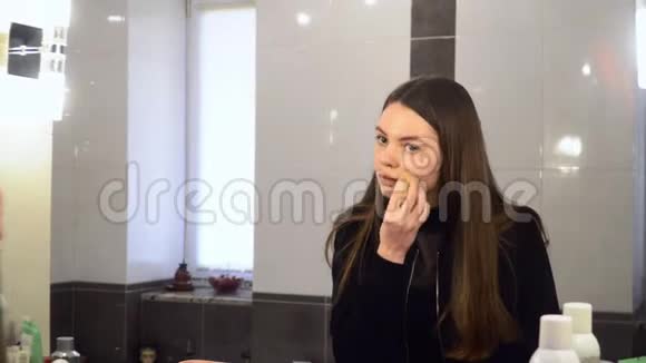 美丽的女人用化妆海绵在脸上微笑和镜子4k视频的预览图