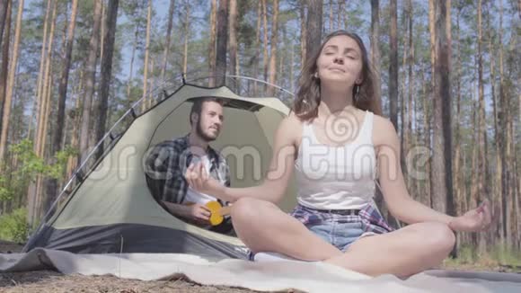 肖像年轻女子在前面沉思而男子在背景上演奏四弦琴坐在帐篷里视频的预览图