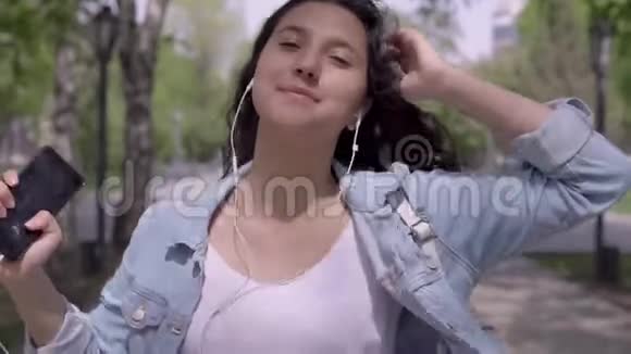 留着长发的滑稽女孩走在街上一边用耳机听音乐一边跳舞特写视频的预览图
