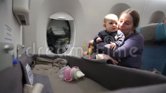 母亲怀着对飞机上第一次飞行的小孩印象深刻一个女人把婴儿抱在怀里拥抱和亲吻视频的预览图