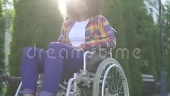 积极的非洲妇女有着非洲发型在轮椅上残疾看着相机微笑着视频的预览图
