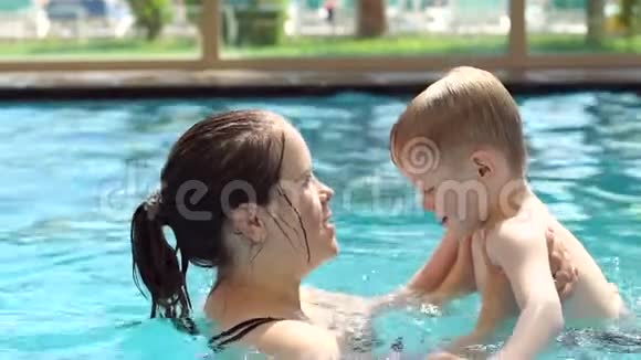 快乐妈妈和她的小儿子在游泳池里游泳亲吻他视频的预览图
