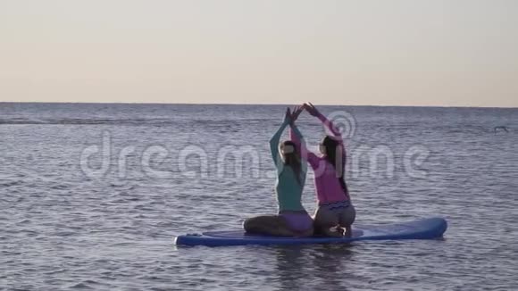 两个女人举起手在冲浪板上摆姿势鸟儿飞过视频的预览图