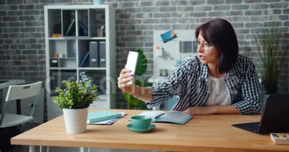 在办公室里用智能手机进行在线视频通话的快乐女人视频的预览图