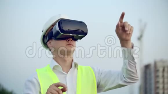 一名男子戴着虚拟现实眼镜头盔和背心在建筑背景下控制着界面的手视频的预览图