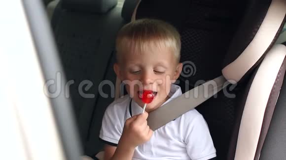 一个可爱的小男孩坐在车里的汽车座椅上吃一根棒棒糖慢动作视频的预览图