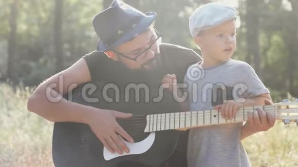 爸爸和小儿子在大自然中间的火炉边弹吉他视频的预览图