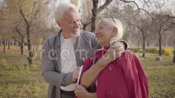 一对快乐的白种人退休夫妇在秋天的森林里站在阳光下拥抱的特写肖像成熟成熟视频的预览图