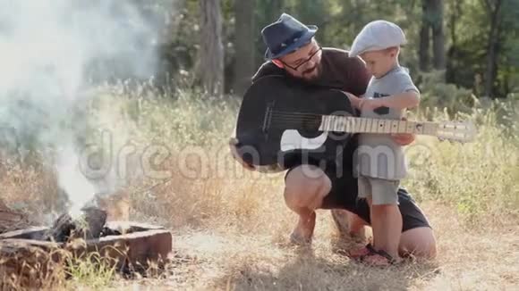 父亲和他的小儿子拿着吉他在森林里野餐视频的预览图