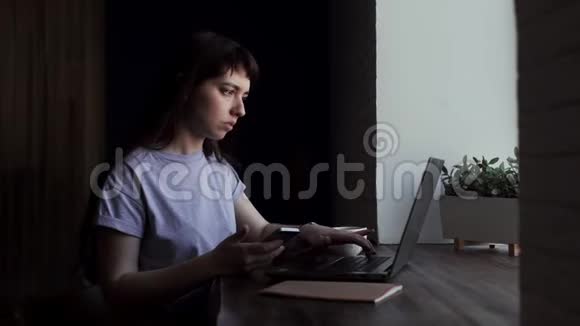 年轻女子看着手机的屏幕近距离的在笔记本电脑上打印视频的预览图