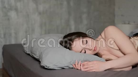 一个年轻漂亮的黑发女人躺在床上睡觉睡觉时翻身伸展身体视频的预览图