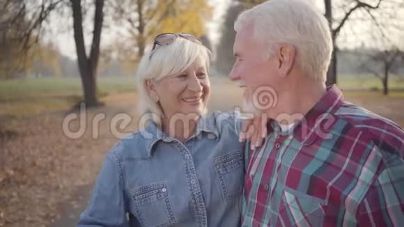 快乐的白种人成熟的家庭互相看着对方微笑着秋天在阳光下站立的欧洲老夫妇视频的预览图