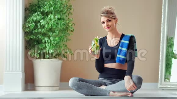 有魅力的健身女性在坐在莲花位置的健身房训练后喝清爽的鸡尾酒视频的预览图