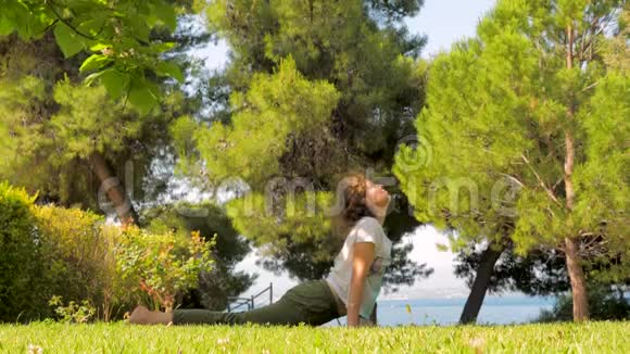 中年妇女在绿草上做瑜伽活泼的女人在海边的绿草上做早操瑜伽视频的预览图