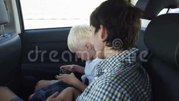 父亲和儿子坐在汽车座椅上玩智能手机而坐在后座上开车视频的预览图