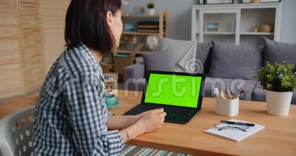 年轻的学生女士在公寓里看着绿色屏幕的笔记本电脑视频的预览图