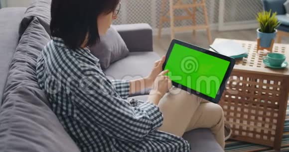年轻女士在公寓里用小工具触摸现代平板电脑的绿色屏幕视频的预览图