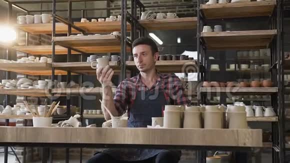 男陶匠在陶器中的工作日里看着手工制作的帽子视频的预览图