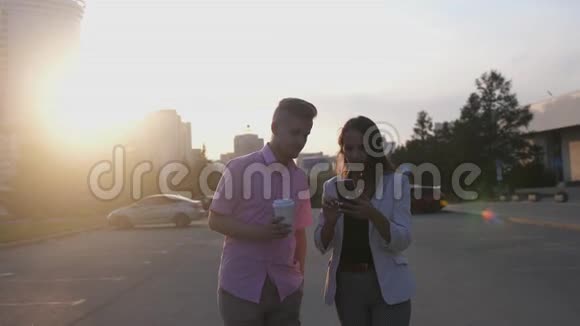 商务夫妇在日落时在街上用手机和咖啡慢动作视频的预览图