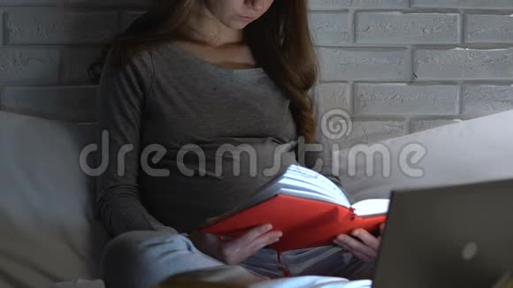 孕妇晚上在笔记本电脑上看书和上网做母亲视频的预览图