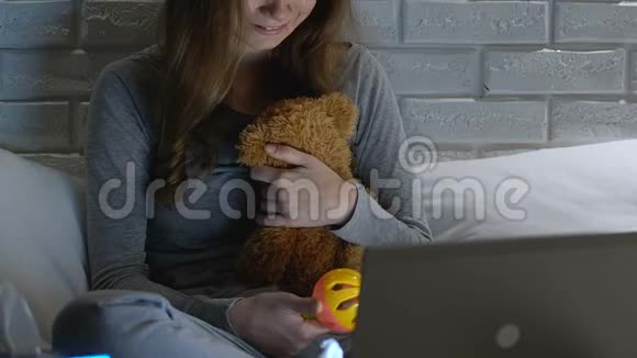 哭泣的女人拿着婴儿玩具和玩具熊在笔记本电脑前不孕视频的预览图