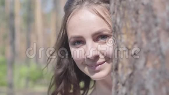 幸福微笑的年轻女子的特写肖像从树干后面看又躲了起来与野生动物团结视频的预览图
