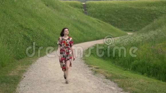 穿着衣服的女孩走在土堆之间的乡村砾石路上视频的预览图