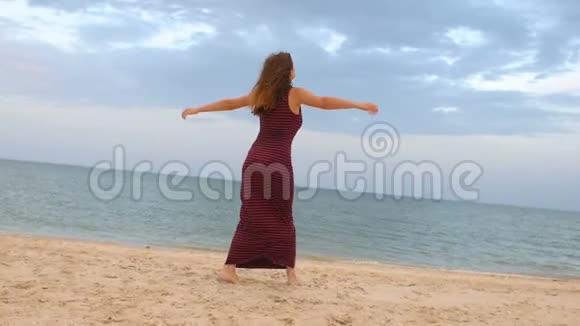 快乐的女孩光着脚穿着裙子在海滩上奔跑旋转跳舞快乐的年轻女子在海边享受生活视频的预览图