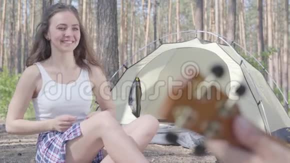 未被认出的男人在帐篷里玩四弦琴而漂亮的年轻快乐的女人坐在他面前可爱的一对视频的预览图