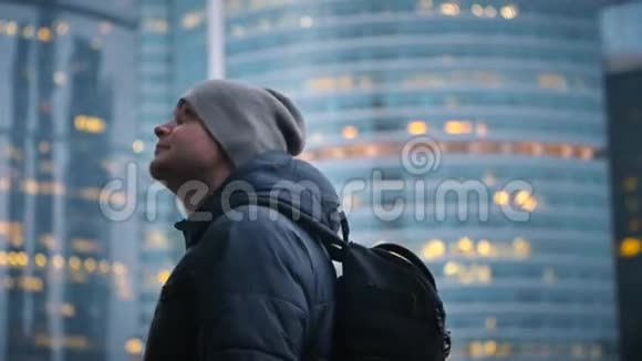 一个带着背包和帽子的年轻人抬头看着摩天大楼起火的背景视频的预览图