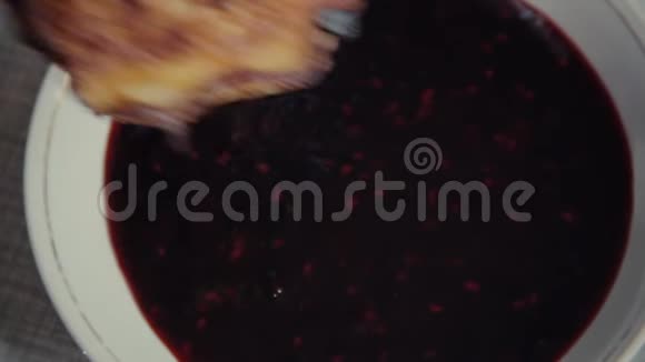 一个新鲜的烤饼用手在两边蘸着黑莓果酱倒入桌上的碟子里视频的预览图