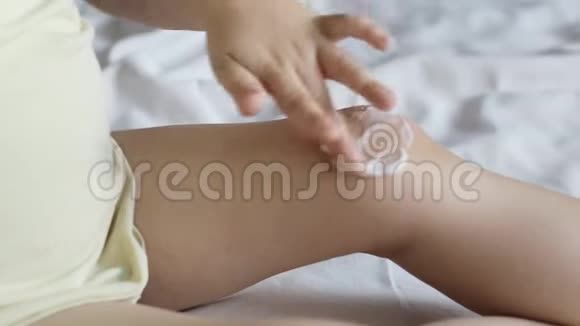 一个小孩用婴儿药膏涂抹他腿上的膝盖婴儿护肤和婴儿霜的概念视频的预览图