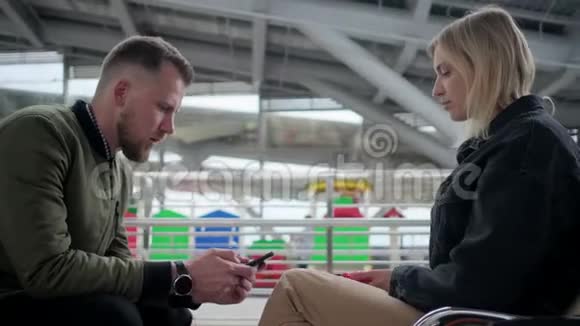 男人和女人坐在出发厅里看着智能手机屏幕视频的预览图