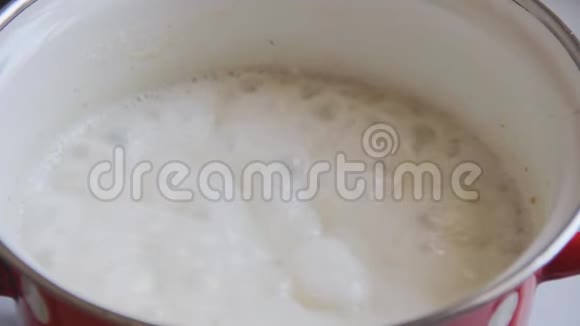 燕麦与牛奶厨师和煮沸在一个红色搪瓷锅在厨房炉子上泡沫聚集在表面煮熟搅拌孔视频的预览图