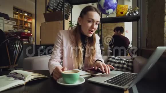 美丽的年轻白种人女人喝咖啡在木桌上的咖啡馆里敲键盘的专题视频的预览图
