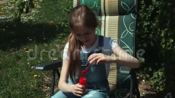 可爱的女孩坐在花园的椅子上吹肥皂泡视频的预览图