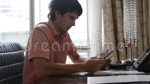 年轻人坐在办公桌前通过互联网从智能手机上的银行卡和喝咖啡进行在线支付视频的预览图