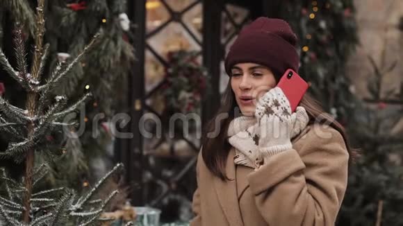 令人惊讶的是穿着冬帽和手套的漂亮女孩在智能手机上说话说哇站着笑视频的预览图