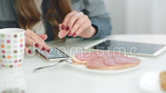在吃三明治时特写女性手滚动手机视频的预览图