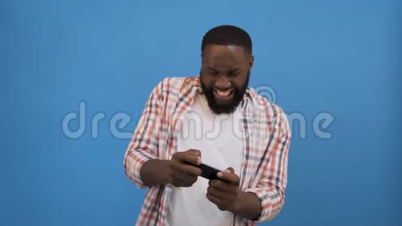 赢得比赛兴奋的非洲男人庆祝成功使用智能手机超过蓝色背景复制空间4视频的预览图