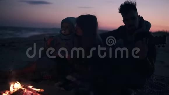 可爱年轻的家庭和女儿一起在海滩上用火和吉他家庭价值观的概念视频的预览图
