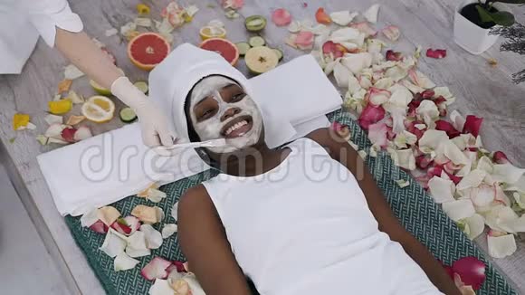 美丽的年轻非洲妇女在温泉度假胜地休息放松而美容学家在她的脸上涂了面膜健康视频的预览图