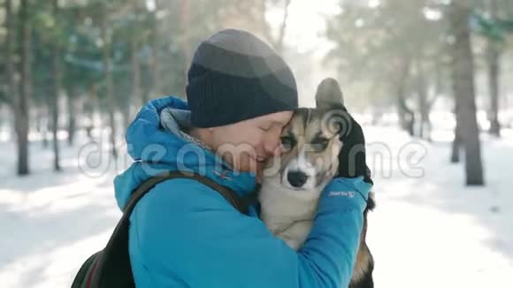 温暖的冬衣中快乐的人的情感肖像在寒冷的阳光下在白雪皑皑的冬公园里抚摸他的宠物视频的预览图
