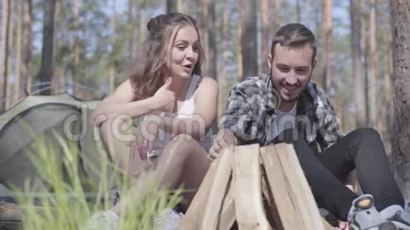 肖像英俊的年轻人在森林里生火而美丽的年轻女子坐在附近可爱的一对视频的预览图