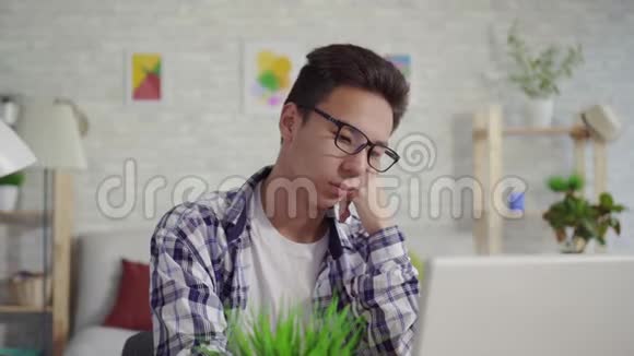 一个穿着衬衫坐在笔记本电脑前的沉睡的亚洲年轻人视频的预览图