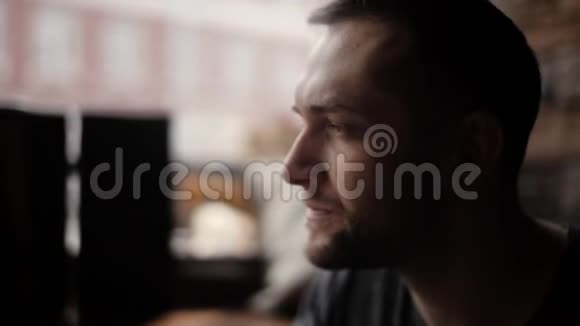 在咖啡馆的一扇窗户旁边坐着一个刚毛的帅哥的特写镜头视频的预览图
