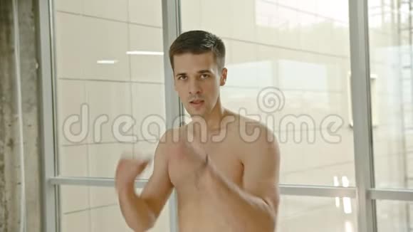 一个半裸运动的拳击手站在窗边对着镜头打拳击视频的预览图