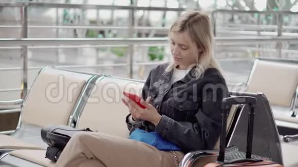 金发女人在机场或火车站的等候区使用智能手机视频的预览图
