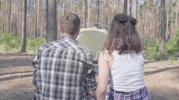 在森林里年轻男女背对着镜头坐在彼此的近旁背景上的帐篷那个人视频的预览图